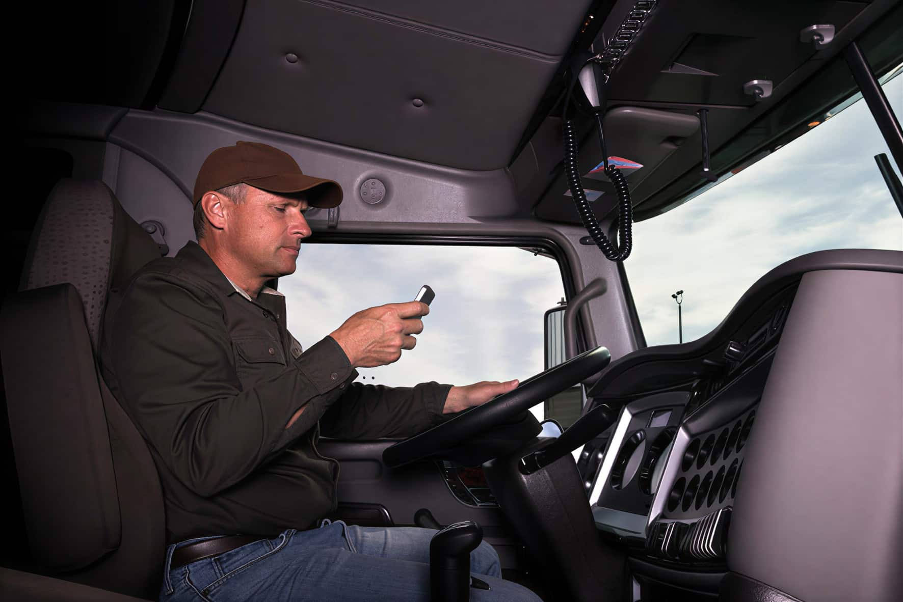 A man seated in a truck cab, holding a device and looking at it intently reflecting on the cause of a truck accident in Austin, TX.
